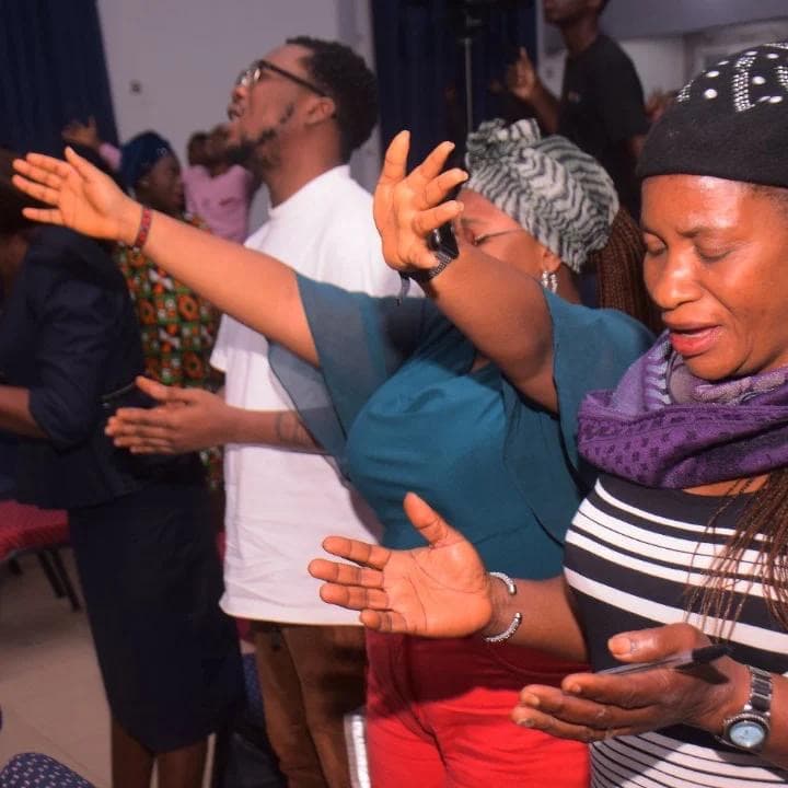 Woman in red with hands raised high, eyes closed, deeply lost in worship